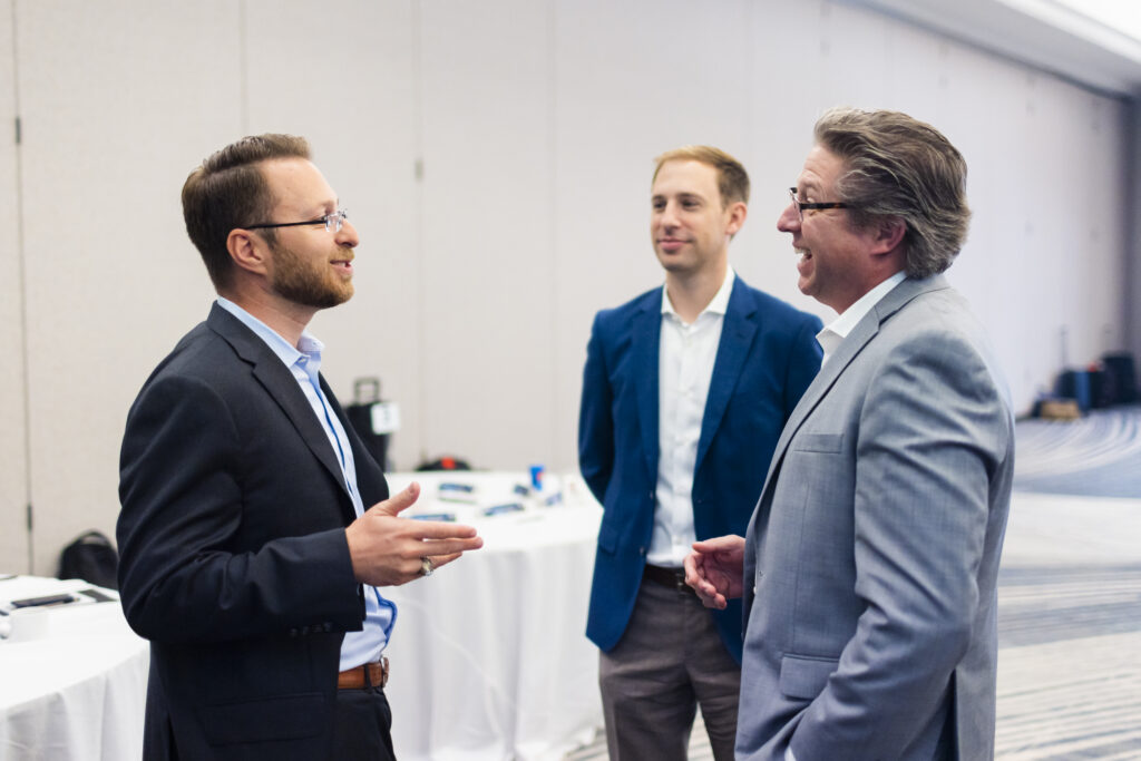 Three professionals speaking during networking or collaboration event in conference setting.