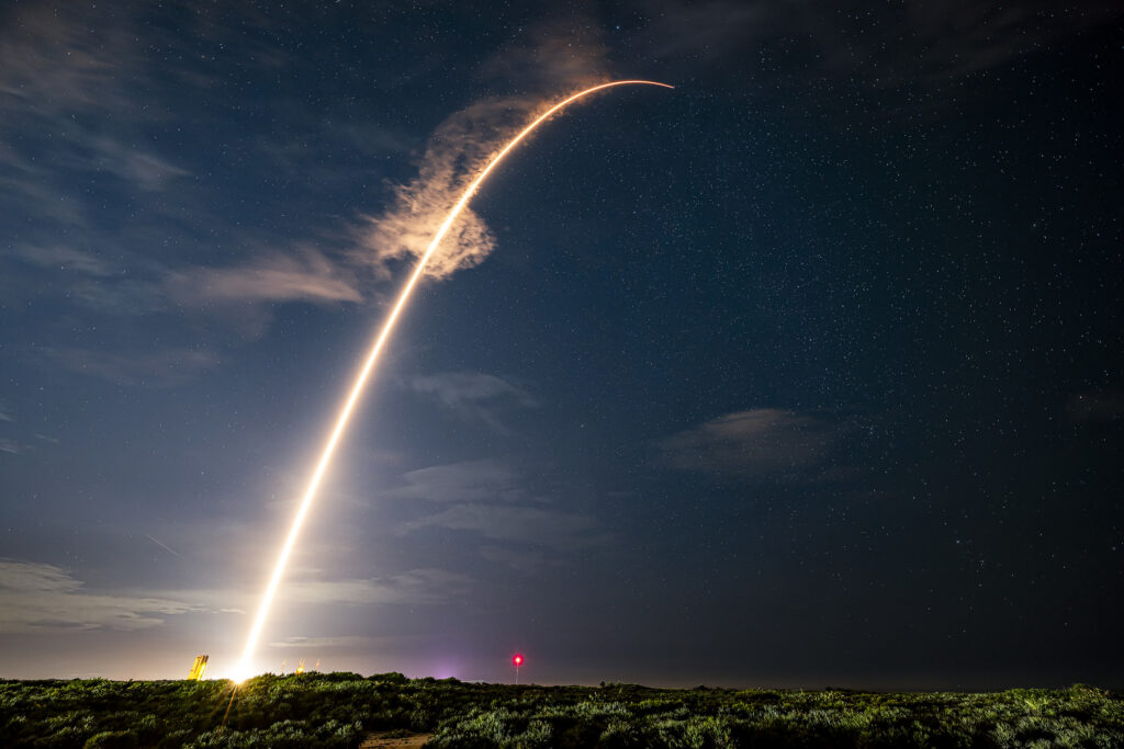 Long-exposure image of rocket launch creating illuminated arc across night sky.