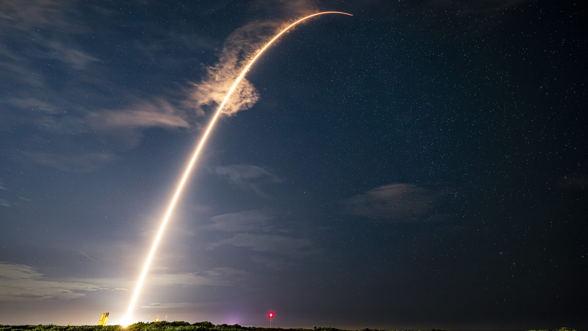 Long-exposure image of rocket launch creating illuminated arc across night sky.
