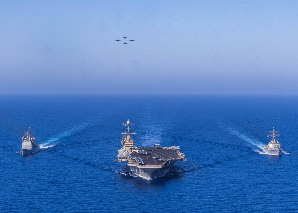 Aircraft carrier operating at sea viewed from aerial perspective.