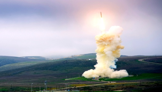 Missile launch with smoke plume rising above a rural test range.