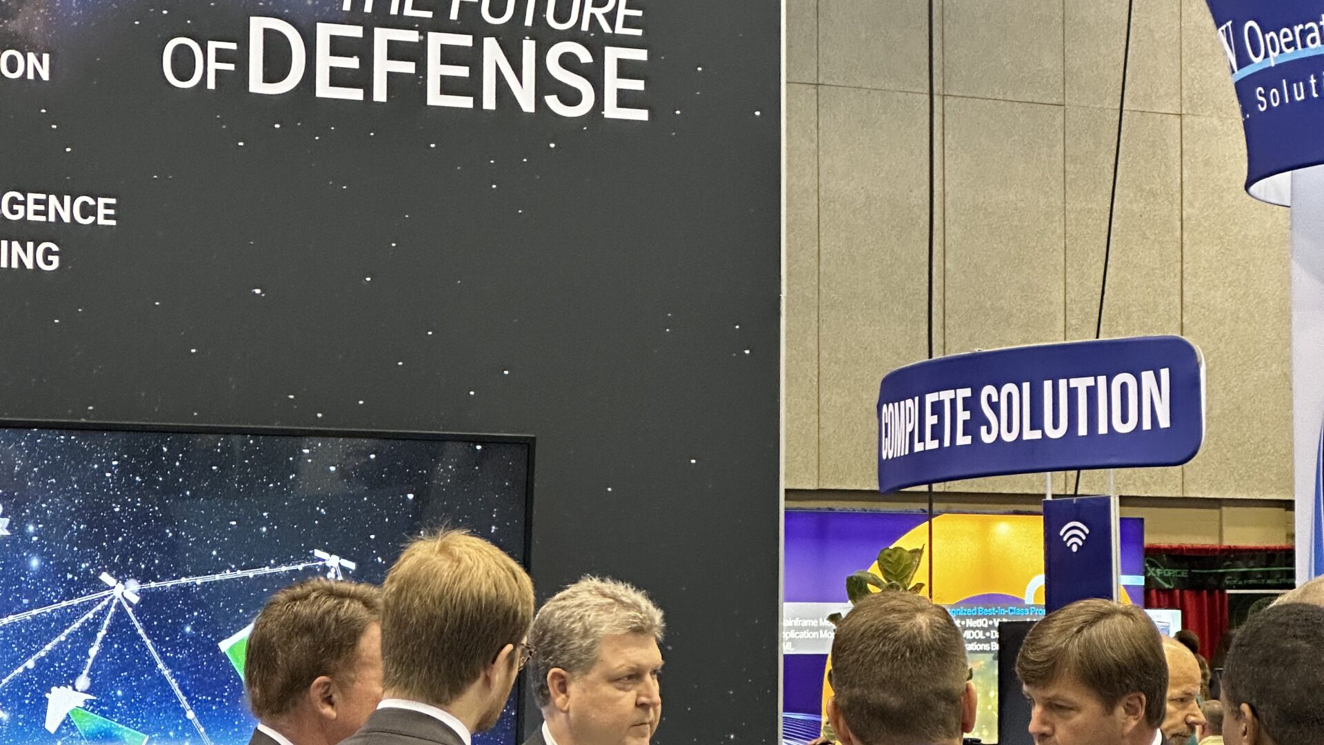 Professionals networking at defense and technology industry conference booth.