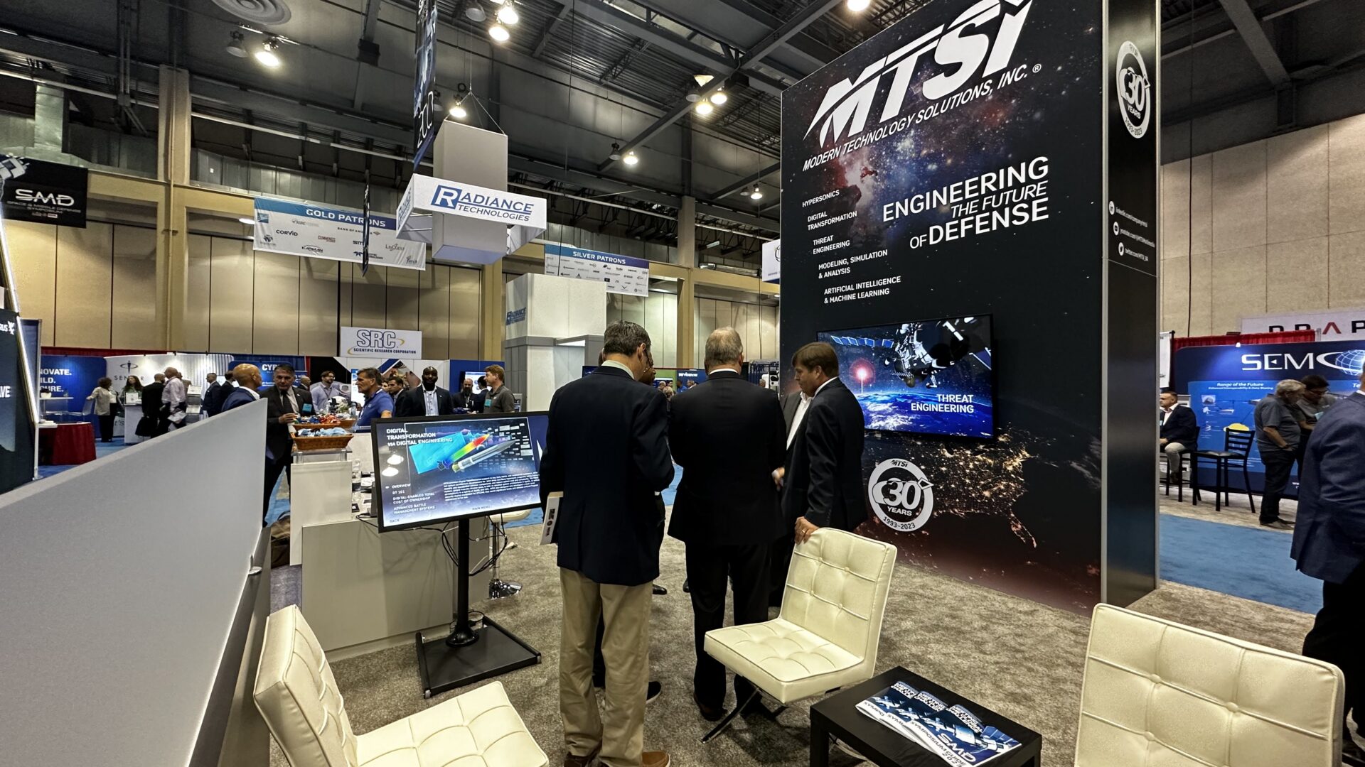 Defense and technology conference booth with attendees networking and reviewing exhibit displays.