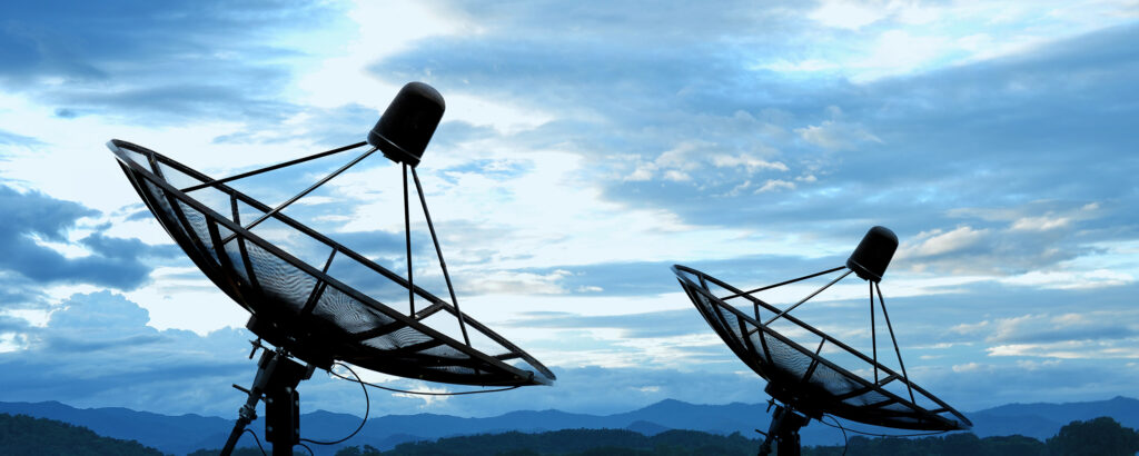 Satellite communication dishes positioned outdoors against cloudy sky.