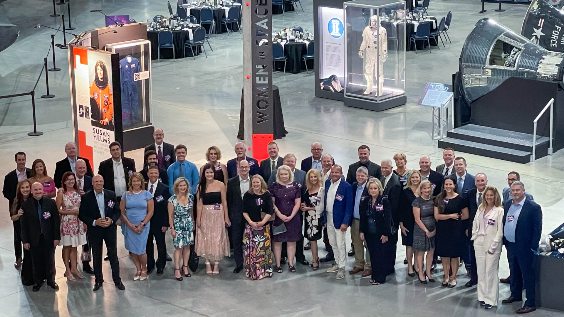 Large group posing inside aviation and space museum during formal event or gathering.