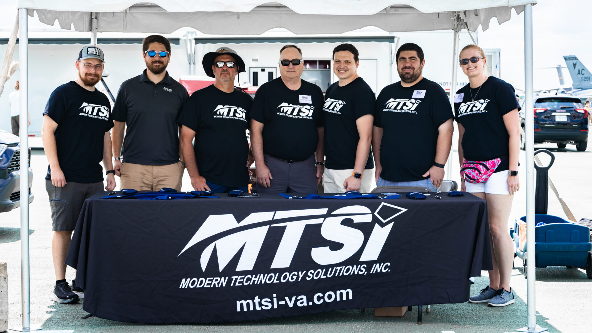 Group of event staff and volunteers posing at outdoor community or aviation event booth.