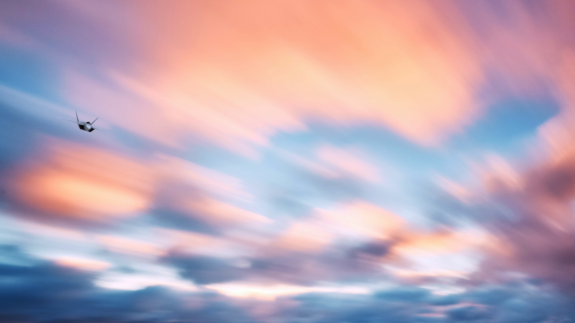 Aircraft flying through colorful cloud formations at sunset.