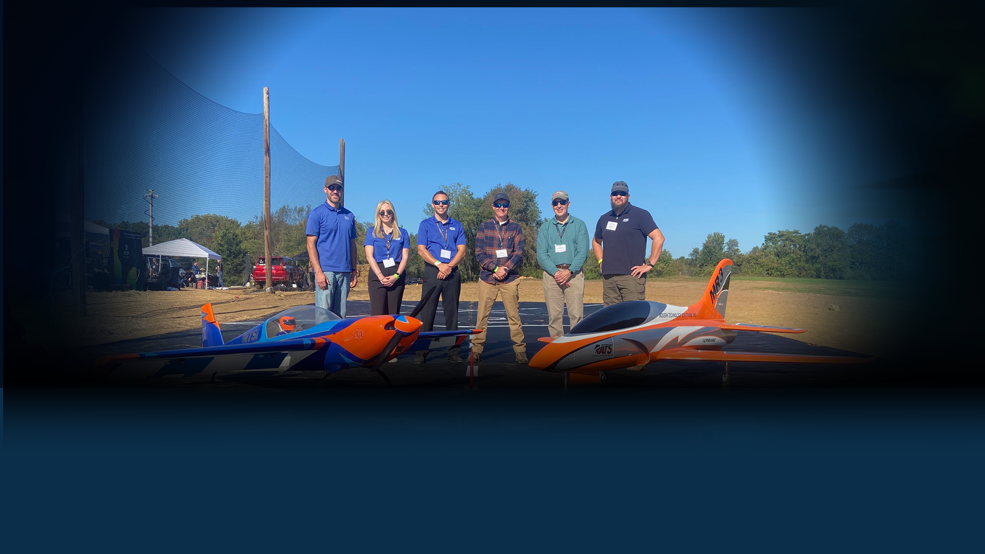 Group standing outdoors beside unmanned aircraft during aerospace testing or demonstration event.