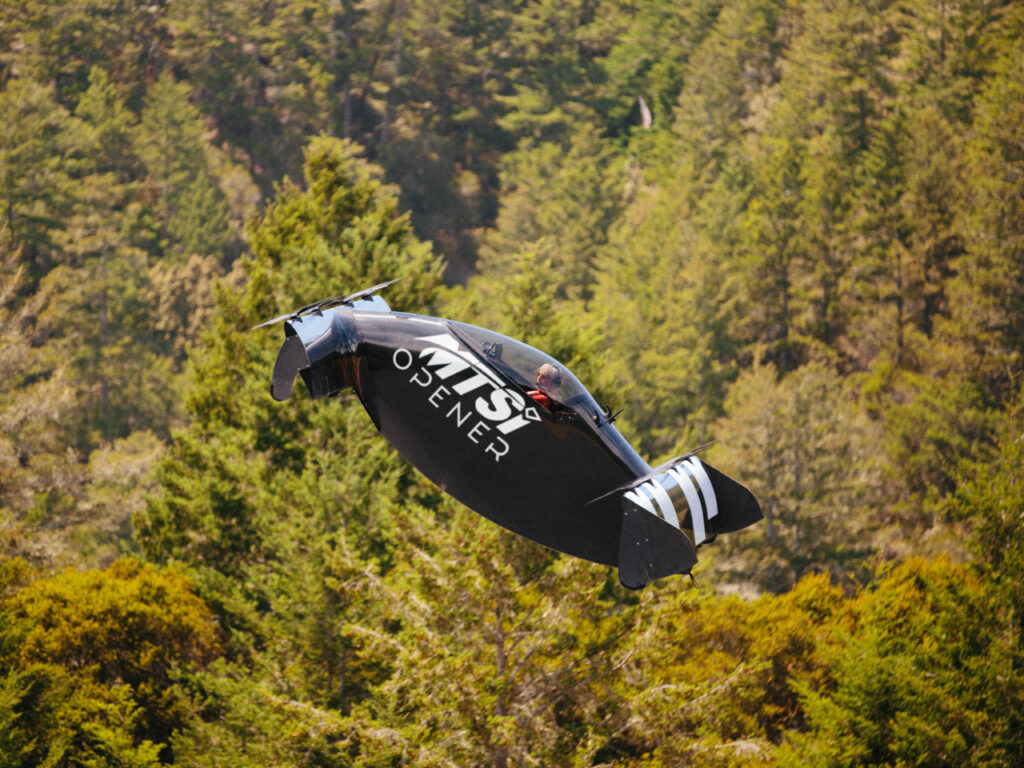 Experimental vertical takeoff aircraft flying above forested terrain.