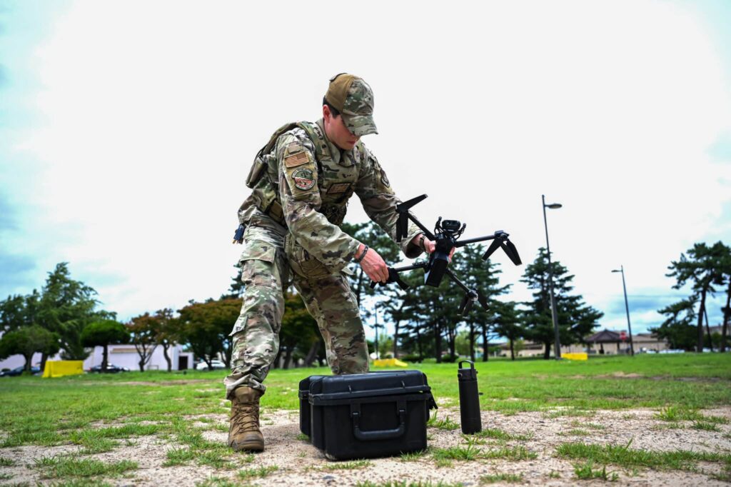 Soldier preparing or operating military tactical equipment in an outdoor environment.
