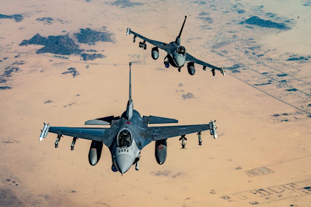 Military fighter aircraft flying in formation over desert terrain.