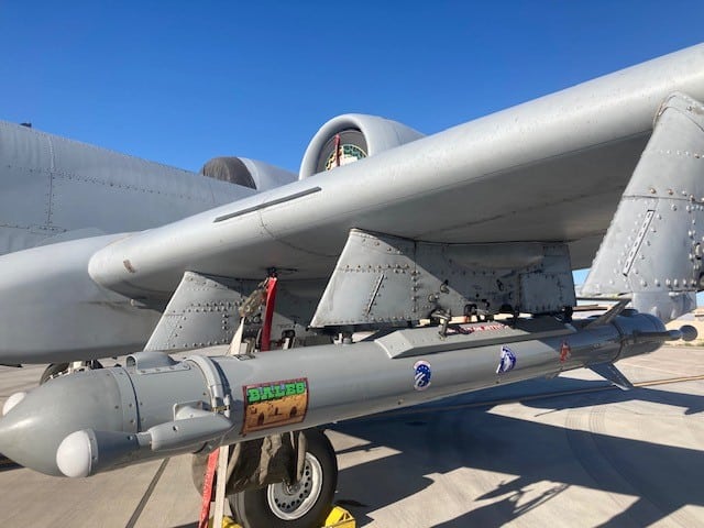 Missile mounted beneath military aircraft wing during ground operations.