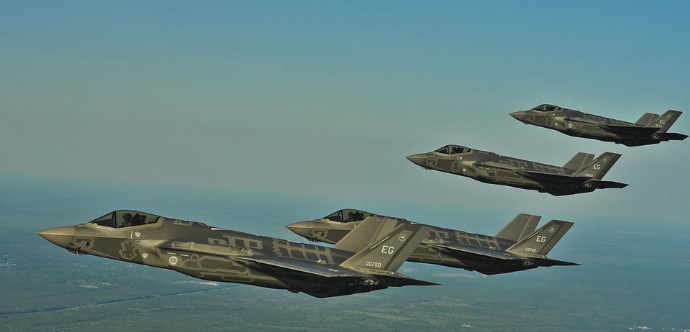 Formation of military fighter aircraft flying in coordinated flight over open landscape.