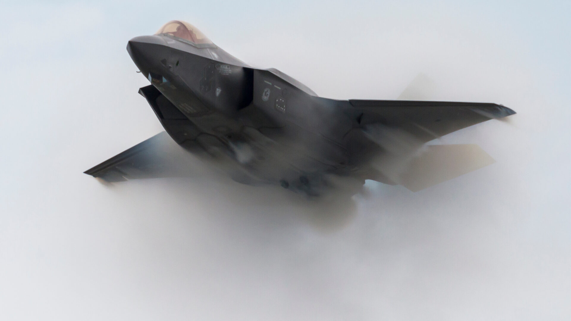 Military fighter aircraft flying through dense cloud vapor during high-speed flight.